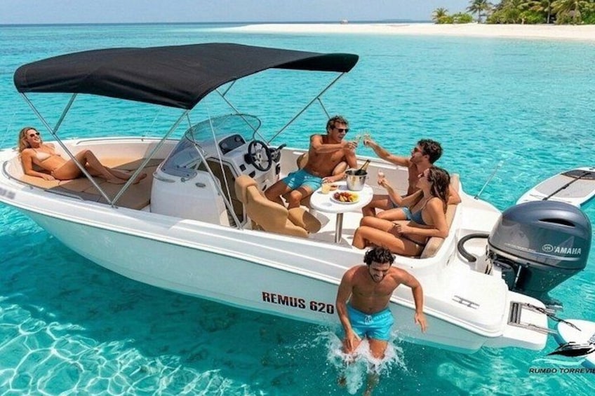 A white motorboat with a black canopy, labeled 'REMUS 620,' on clear turquoise water. 3