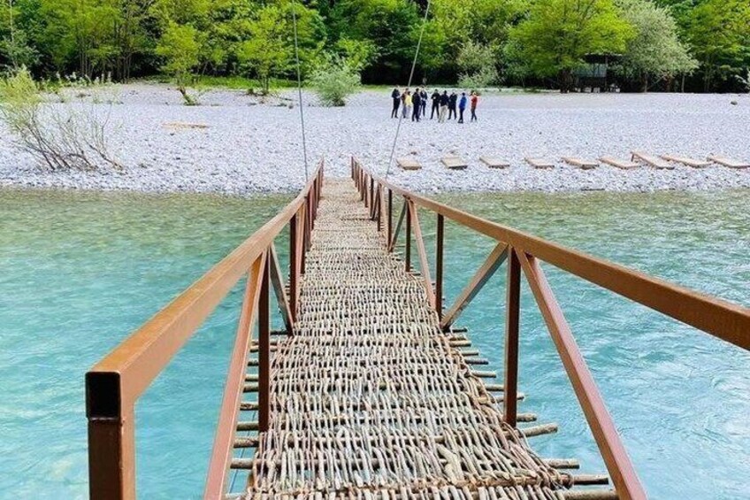 A wooden bridge over clear water with people in the background. 3
