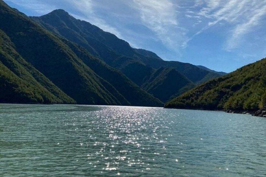 A calm lake surrounded by lush green mountains under a clear sky. 5