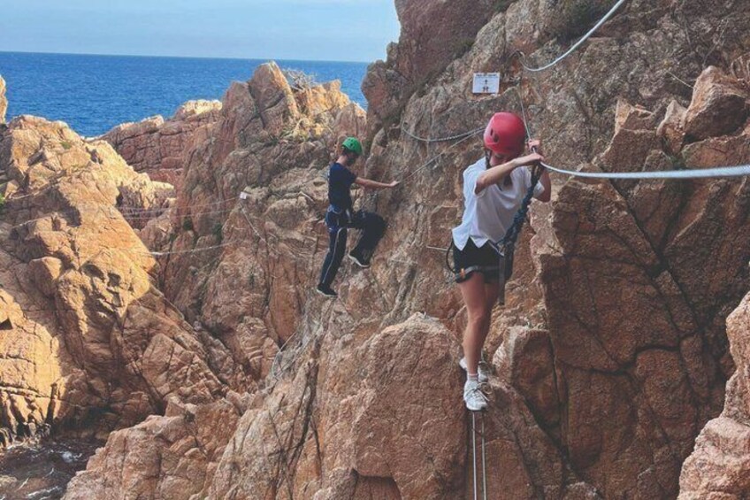 Two people rock climbing on a rocky cliff with a rope, overlooking the ocean. 2