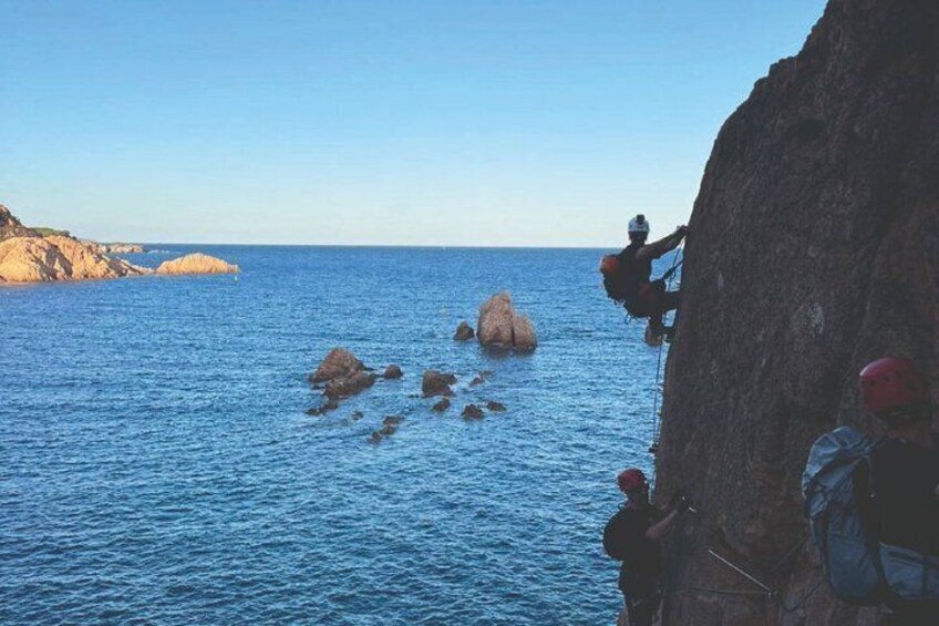 A person climbing a cliff by the sea, with calm waters and distant rocky formations. 3