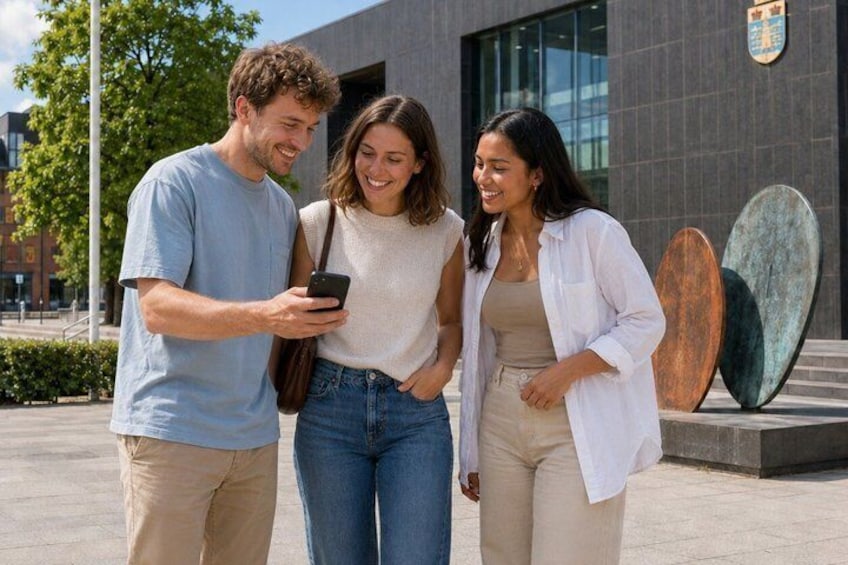Three people standing on a sidewalk, one holding a smartphone, with surfboards in the background. 3