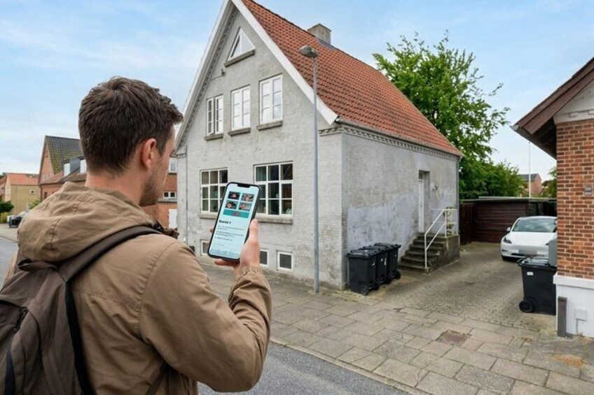 A person using a smartphone in a residential area with a house and parked cars. 2