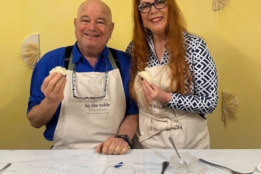 Two people wearing aprons with 'by the table' text, standing at a table with a spoon and a bowl. 3