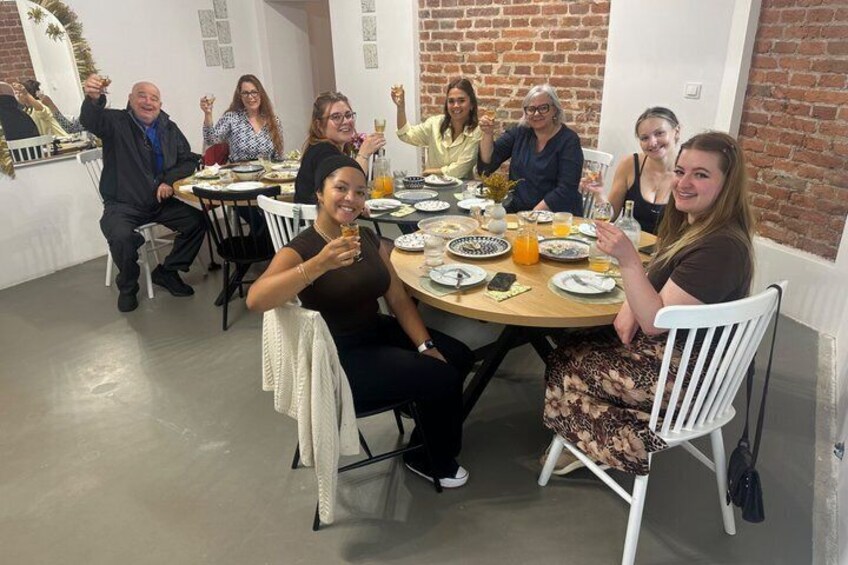 A group of people seated around a round table in a room with brick walls and white chairs. 2
