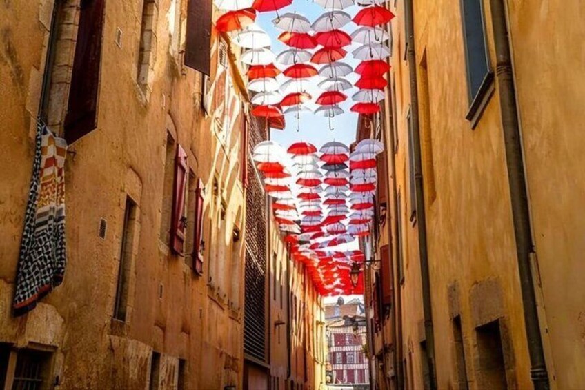 A narrow street with buildings on either side and a canopy of red and white umbrellas overhead. 3