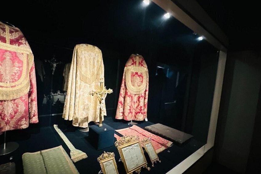 A display case with three ceremonial robes, a candelabra, and a framed picture. 3