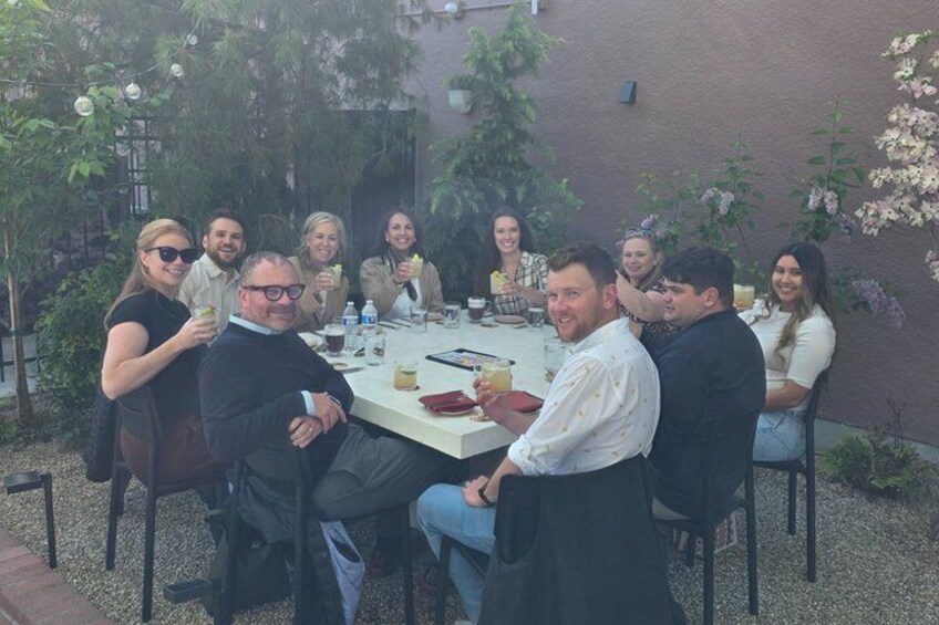 A group of people seated around a table outdoors, engaged in conversation. 2