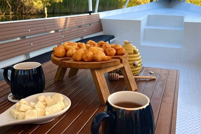 A wooden table with a plate of pastries, a honey jar, and two mugs on a deck. 2