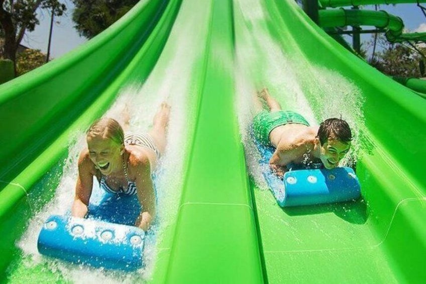 Two people sliding down a green water slide using blue floats. 2