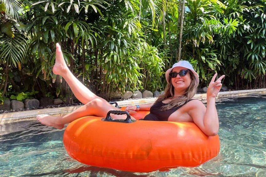 A person floating on an orange inflatable tube in a pool surrounded by tropical plants. 2