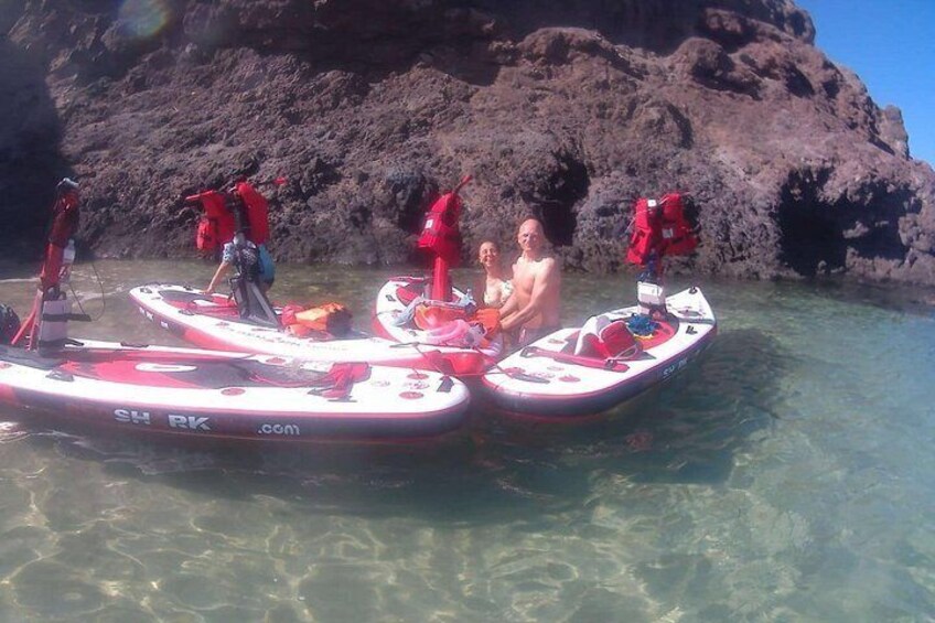 Three kayaks with people in them, a rocky shoreline, and clear water. 4