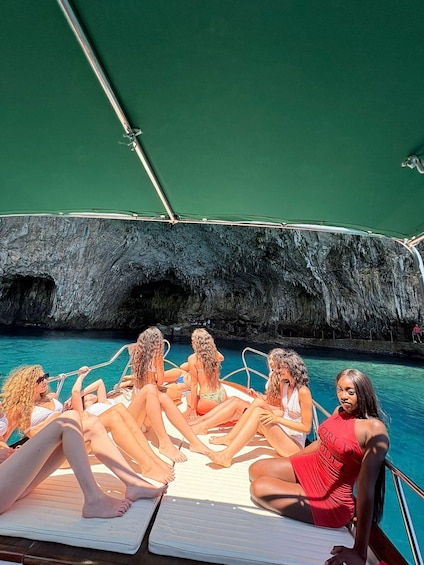 A group of people relaxing on a boat deck by a rocky cliff. 1
