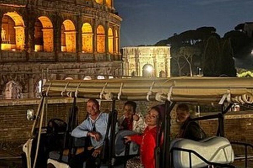 A golf cart with passengers near a historic building at night. 1