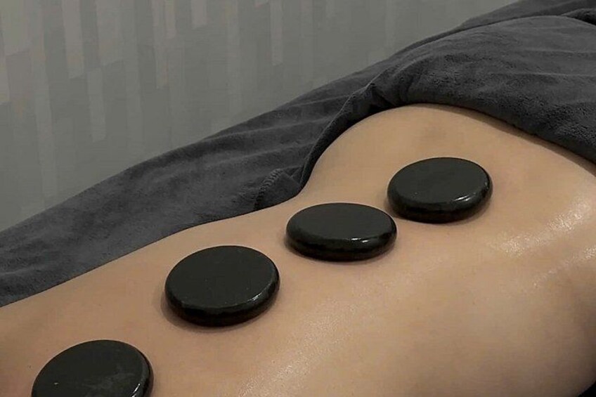 A person receiving a therapy with black stones placed on their back. 1