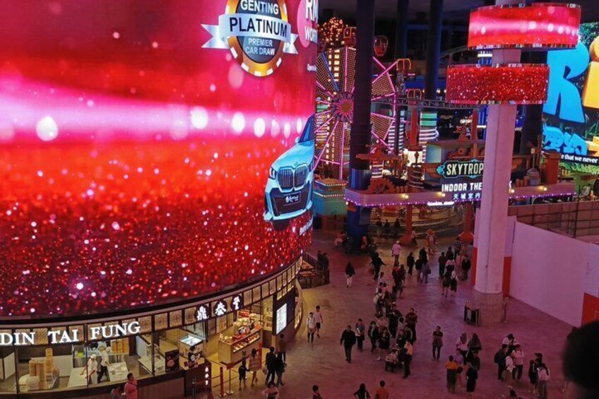 A brightly lit indoor amusement area with a Ferris wheel, a BMW car display, and a crowd of people. 3