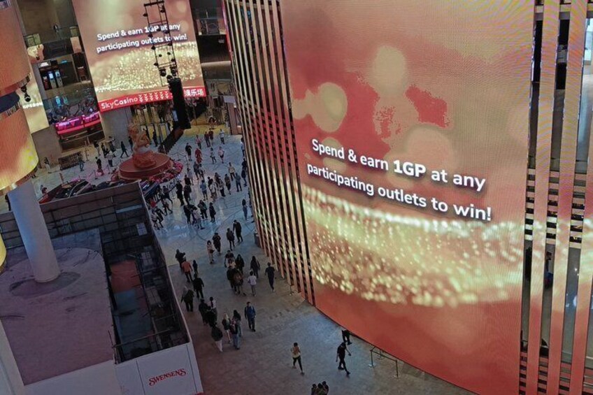 A crowded indoor space with large digital screens displaying promotional content. 5