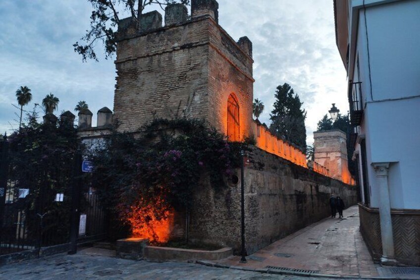 A historic stone wall with a lit-up tower and a pathway leading through it. 2