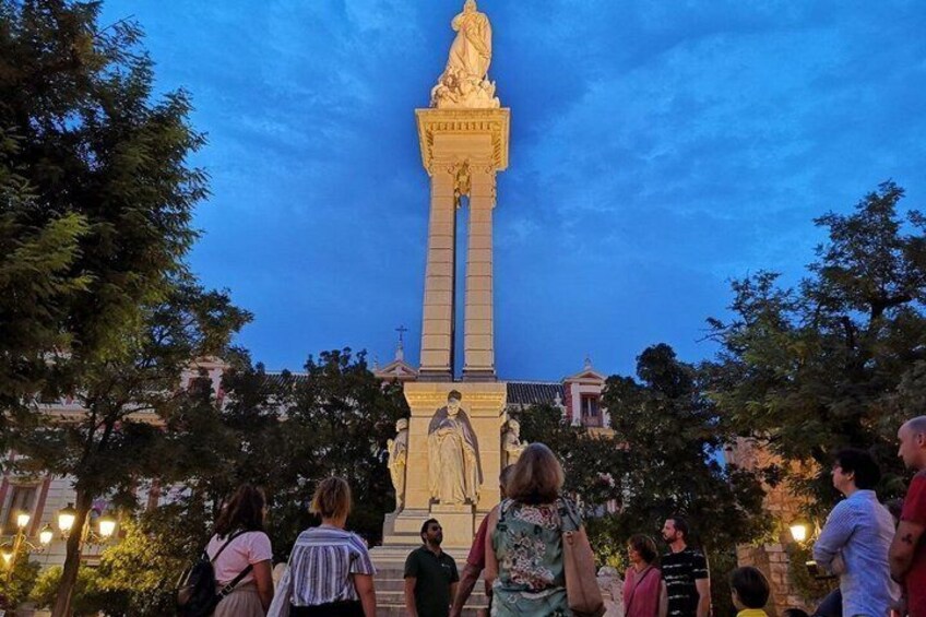 A monument with a statue, surrounded by trees and people. 3