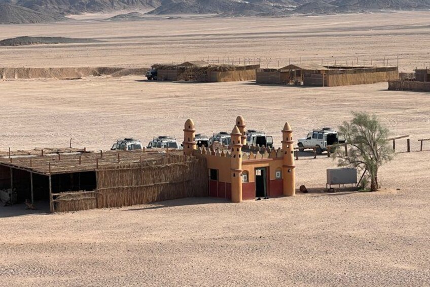 A desert landscape with a small building with a tower, surrounded by vehicles and sparse vegetation. 2