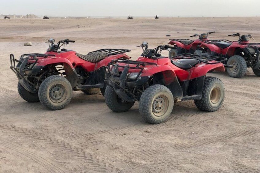 A row of red quad bikes parked on a sandy terrain with a flat horizon in the background. 2