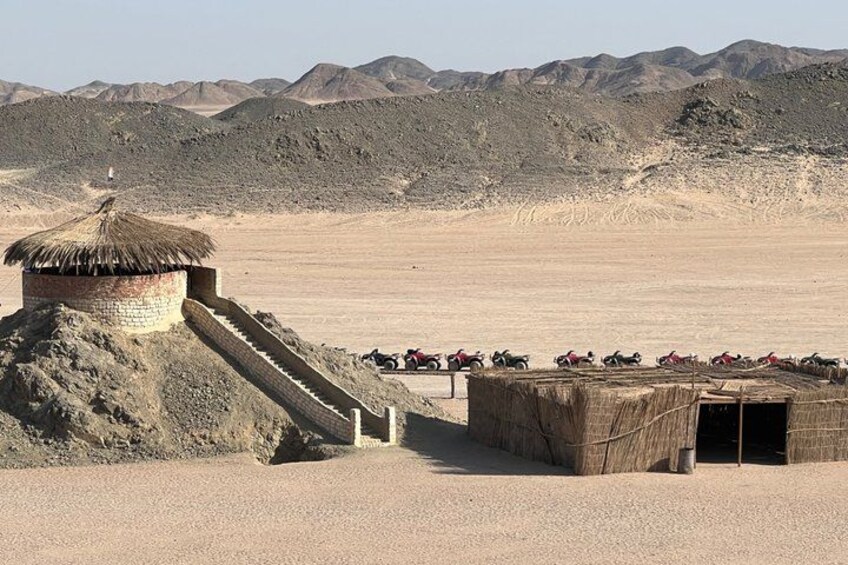 A desert landscape with a small structure with a thatched roof, a stone staircase, and a group of people on motorcycles. 3