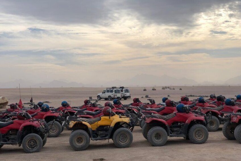 A group of off-road vehicles parked on a sandy terrain with a cloudy sky in the background. 5