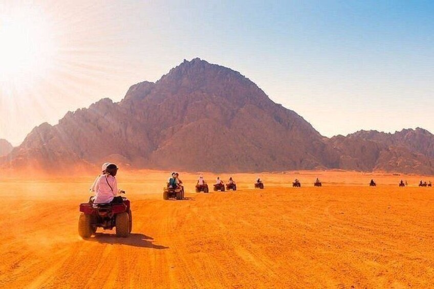 A group of people riding quad bikes in a desert with mountains in the background. 3