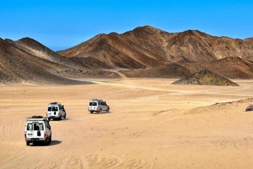 Three off-road vehicles in a desert landscape with mountains in the background. 2