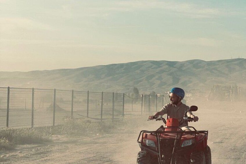 A person riding a quad bike on a dirt road with a fence and hills in the background. 1