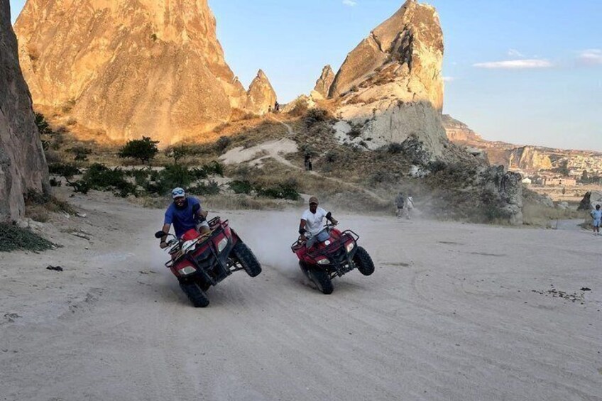 Two people riding ATVs on a dirt road with large rock formations in the background. 4
