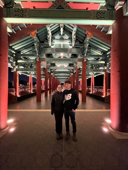 A couple standing under a traditional Japanese torii gate at night. 3