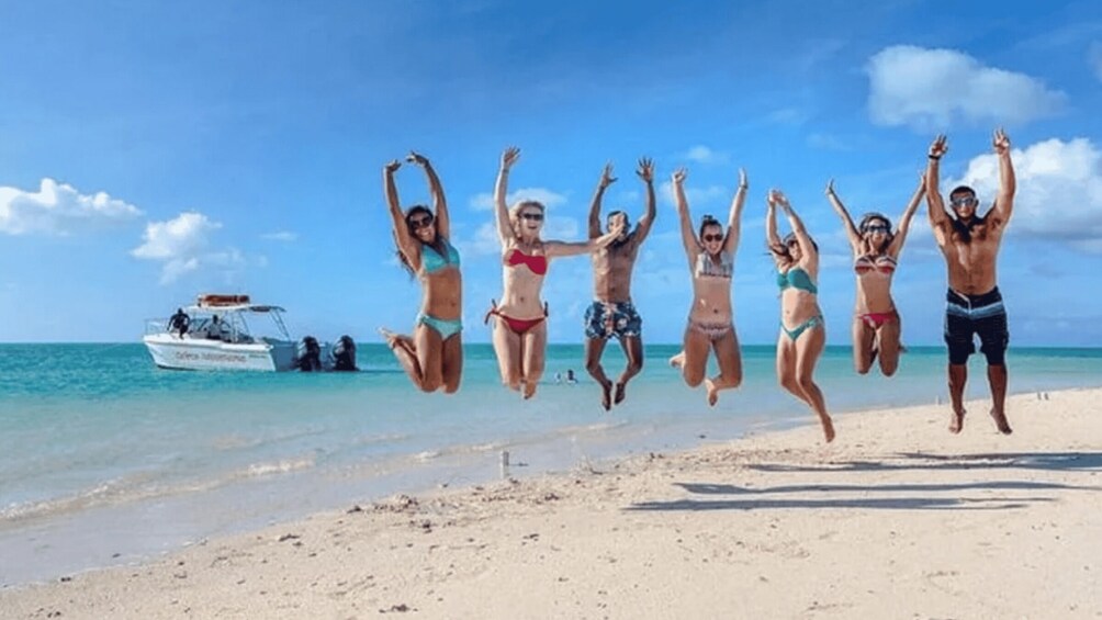 A group of people jumping on a beach with a boat in the background. 5