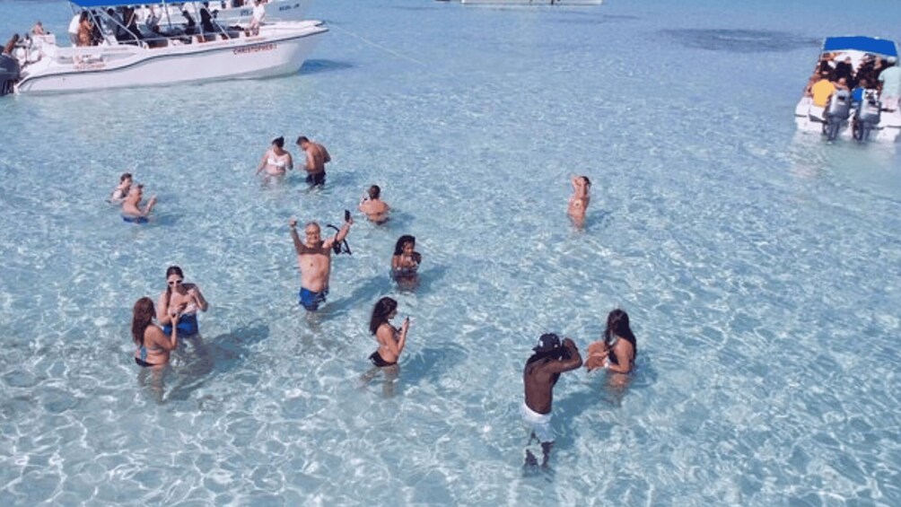 People swimming in clear shallow water with boats in the background. 4