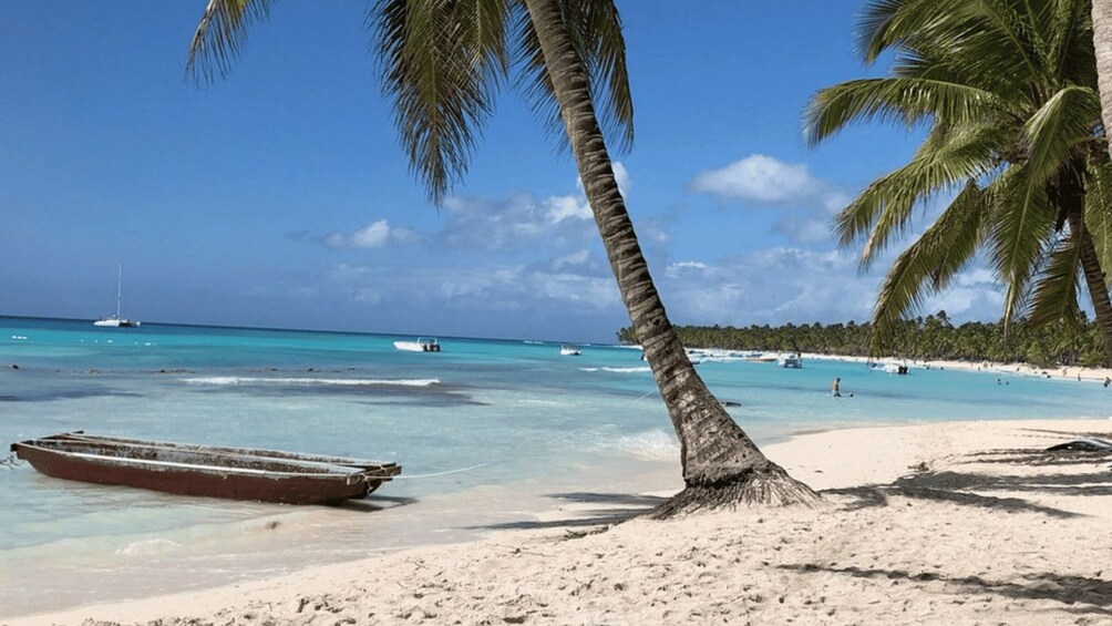 A beach with clear turquoise water, a boat on the shore, and palm trees. 2