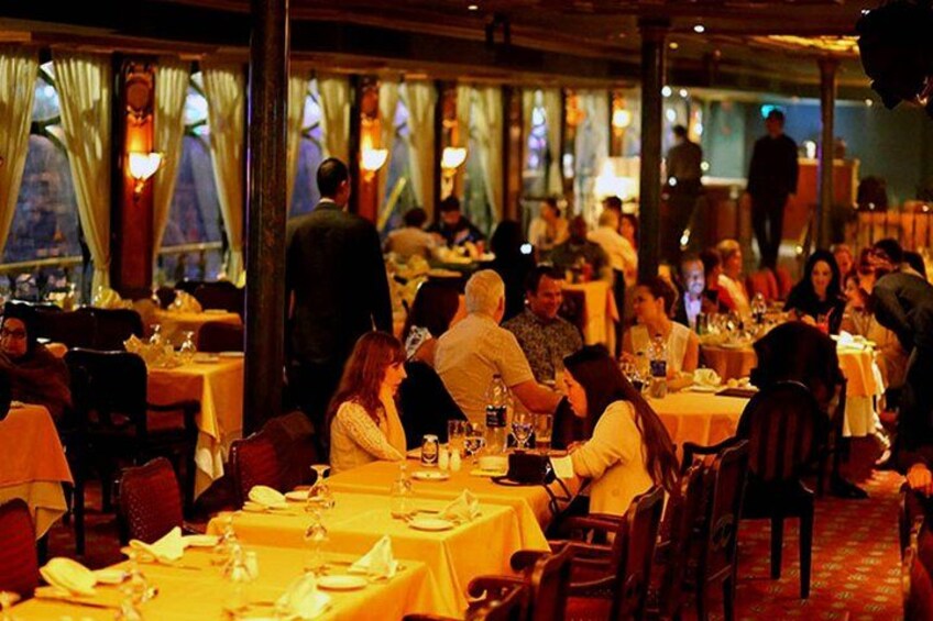 En livlig restaurant med dækkede borde, siddende gæster i samtale og en varm, svag belysning. 2
