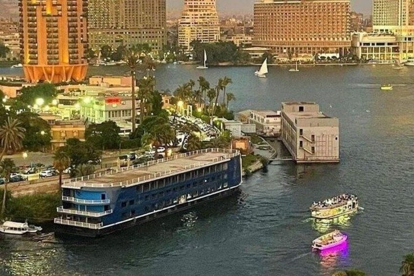A river with a large blue boat, smaller boats, and buildings along the riverbanks. 2