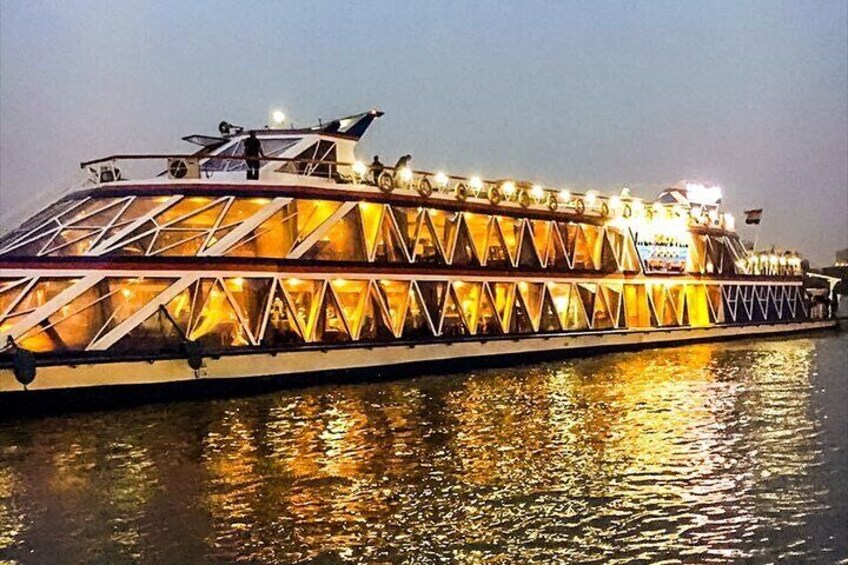 A large, illuminated riverboat with a distinctive triangular window pattern and a flat deck. 1