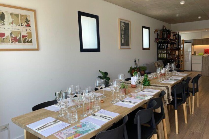 A long dining table set for a meal with chairs, framed pictures on the wall, and a kitchen in the background. 3