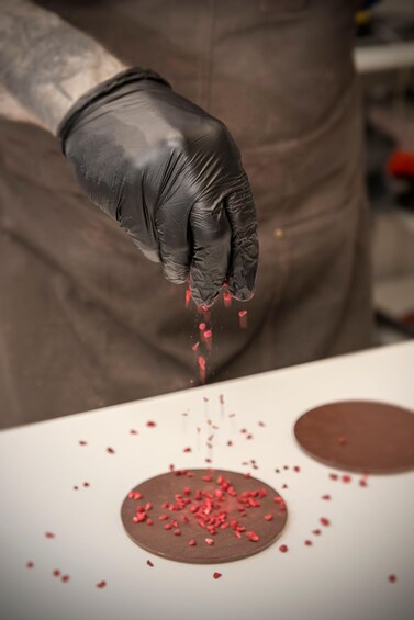 A gloved hand sprinkling red powder onto a chocolate surface. 4