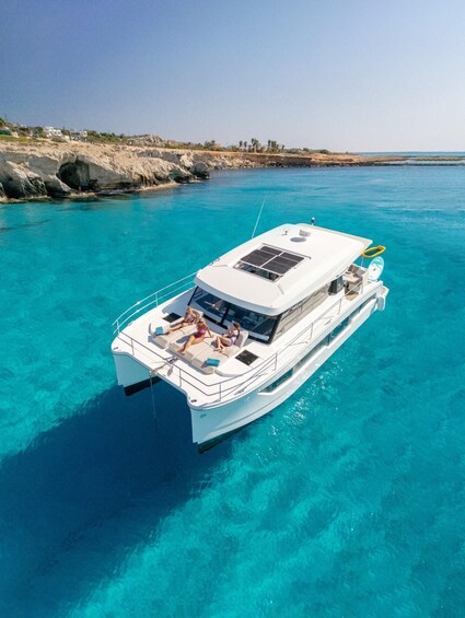 A white boat with passengers on a clear turquoise sea, rocky shoreline in the background. 1