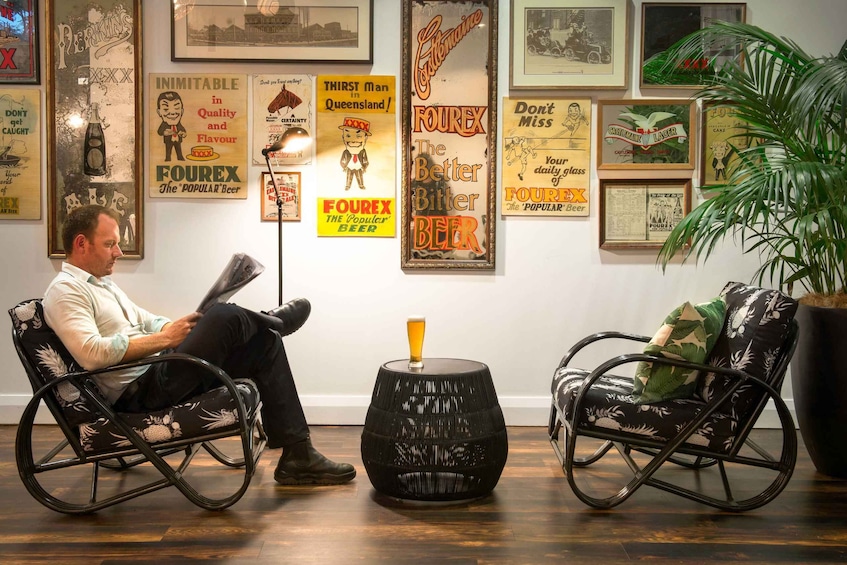 A man reading in a chair, a wooden barrel stool, and vintage beer posters on the wall. 4
