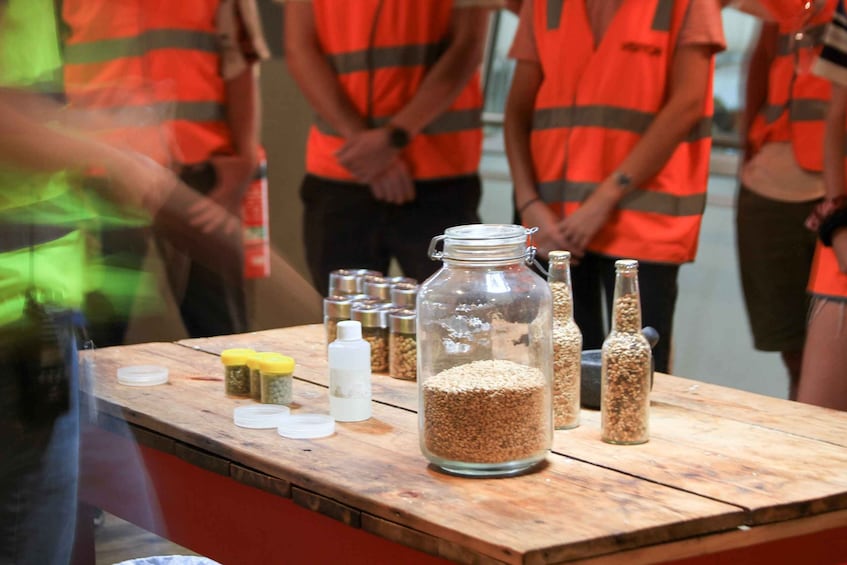 A table with jars of grains and spices, and people in orange vests standing behind. 5