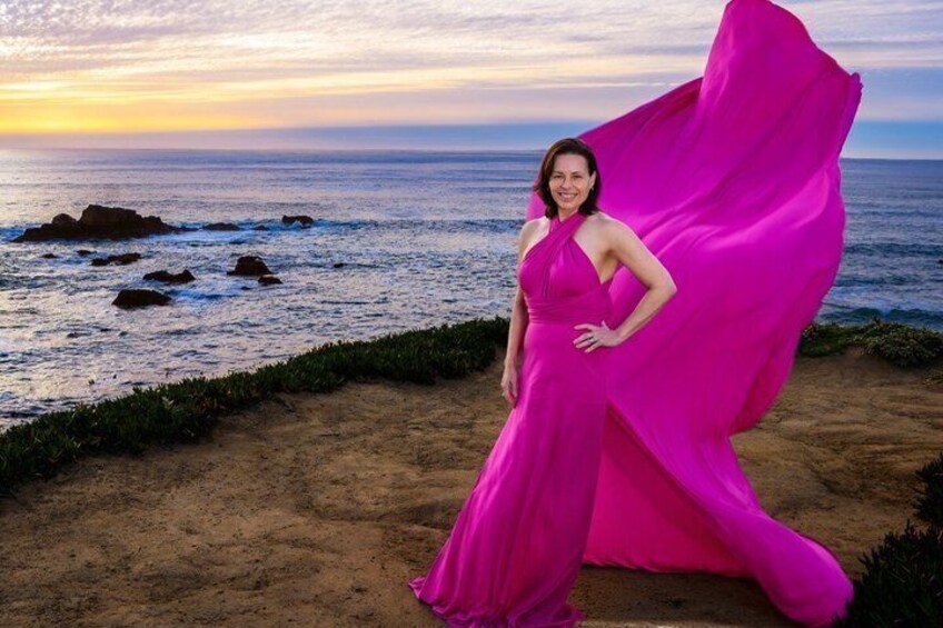 A person in a pink dress standing on a beach with the ocean and rocks in the background. 5