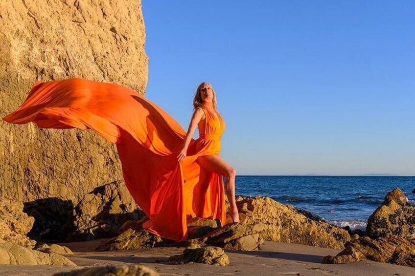 A person in an orange dress sitting on rocks by the sea. 4