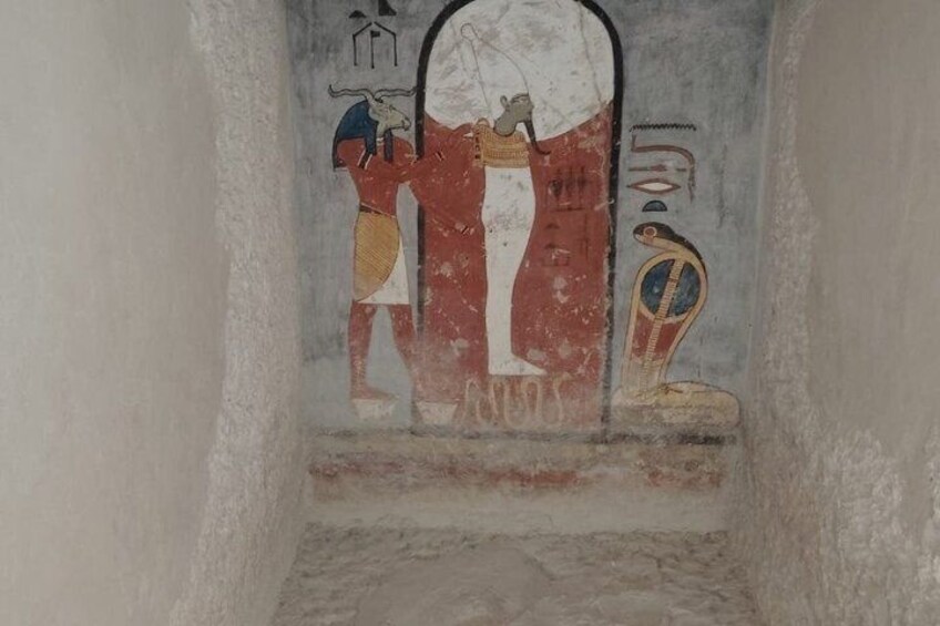 An ancient Egyptian wall with a fresco depicting a figure in a red and white garment, a blue and gold headdress, and a hieroglyphic inscription. 5