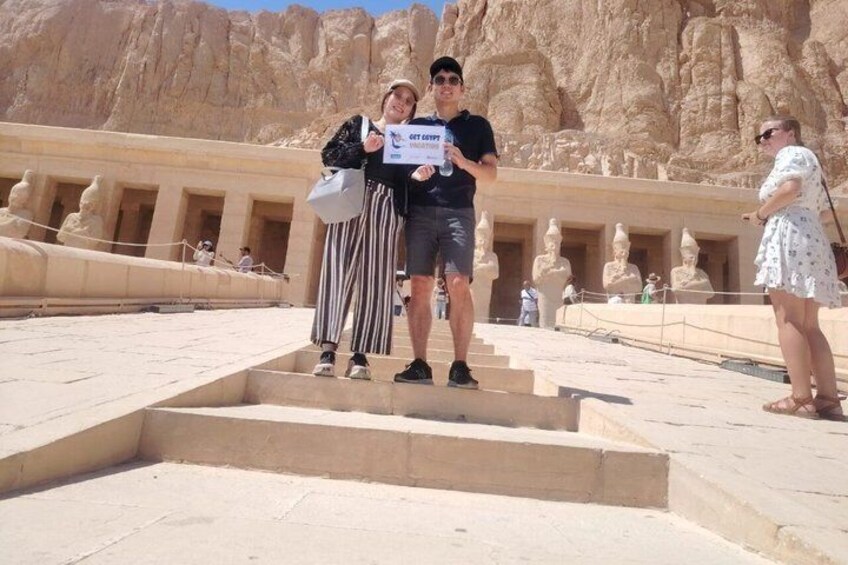 A person holding a sign in front of an ancient Egyptian temple with steps and statues. 2