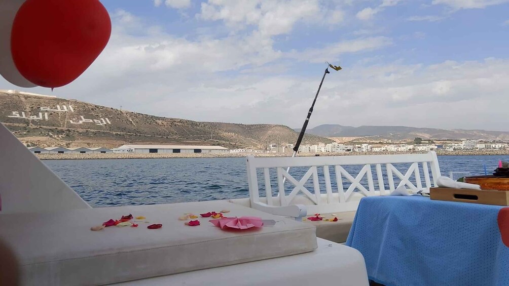 A boat deck with a fishing rod, a white railing, and a coastal landscape with buildings in the background. 5