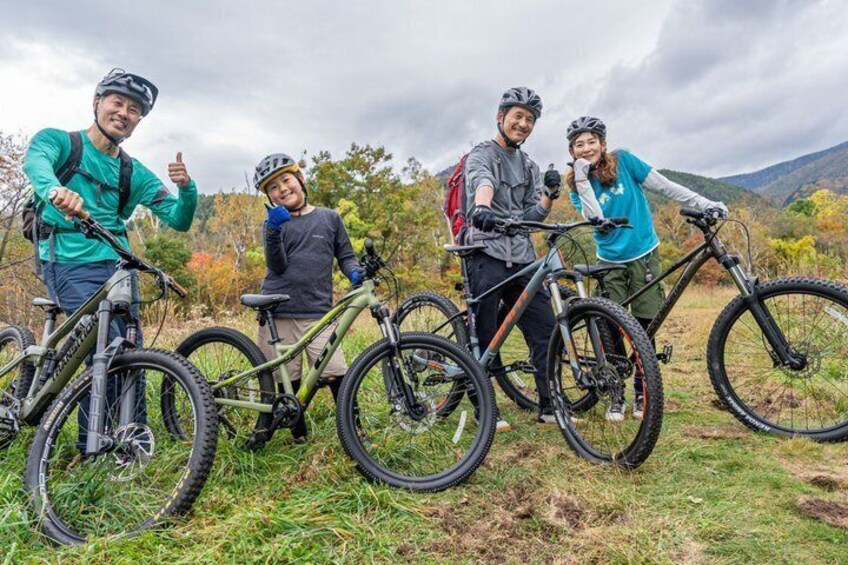 Four people with bicycles in a grassy field with mountains in the background. 4