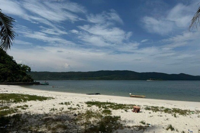A beach with white sand, calm water, and distant mountains. 5